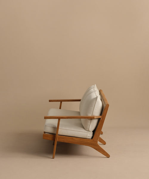 The Outdoor Vista Sofa features a minimalist wooden frame with modern angled lines and light beige Tempotest cushions, shown against a plain beige background.
