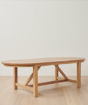 The Montecito Oval Dining Table, handmade from solid white oak with sturdy legs and a crossbar support, sits elegantly on a light wood floor against a plain white wall.