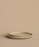 A pair of round beige stoneware dinner plates—a Pacific Salad Plate stacked inside a larger one—arranged on a plain beige background.