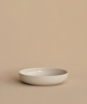 A simple, round, shallow white Pacific Soup Bowl is displayed on a beige surface against a matching background, highlighting its minimalistic, pattern-free elegance.