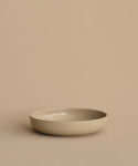 The Pacific Soup Bowl is a plain, shallow beige stoneware piece displayed on a matching beige surface with a neutral beige background.