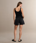 A woman faces away, wearing a black sleeveless top, the Parker Long Short by AGOLDE in a vintage denim fit, and black sandals, set against a plain beige background.