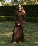 A woman with long hair stands barefoot on grass, wearing the Penelope Skirt. She is outdoors, with hedges and trees in the background.