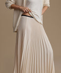 Person wearing a long ivory pleated skirt and white top on a beige background