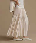 Person wearing an ivory pleated skirt and white top against a brown background