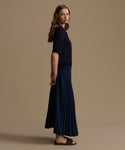 Woman wearing a navy top and navy pleated skirt against a beige background