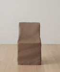 A brown, fabric-covered chair with a boxy design sits on a light wooden floor against a white wall, protected by the Outdoor Montecito Dining Chair Cover for UV resistance, lasting durability, and style.