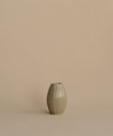 A small ribbed ceramic vase in a muted sage green-gray glaze, centered against a solid warm beige background.