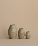 Three ribbed ceramic vases in a light beige-gray glaze, arranged by size against a solid warm beige background.