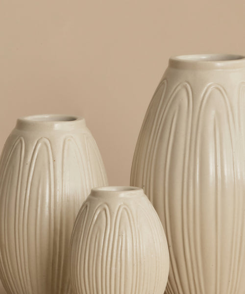 Three ribbed ceramic vases in a warm cream-beige color, arranged against a solid beige background.