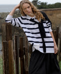 Woman wearing a navy stripe post pullover standing outdoors by a wooden fence.