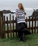 Woman in a Navy Stripe post pullover worn by a person with a neutral background and black skirt standing by a wooden fence with ocean in the background