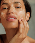 A close-up of a person applying Pure Gel Cleanser to their face, gently touching their cheek. Their dewy, well-lit skin suggests a brighter complexion, while their expression remains neutral.