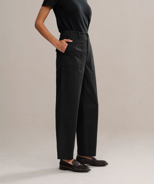 A person in black Ranger Trouser, a black short-sleeve shirt, and black loafers stands with hands in pockets against a plain light-colored background.