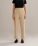 A person in a black short-sleeve shirt, Ranger Trouser in beige with front pockets and a fitted silhouette, and black loafers stands against a plain beige background.