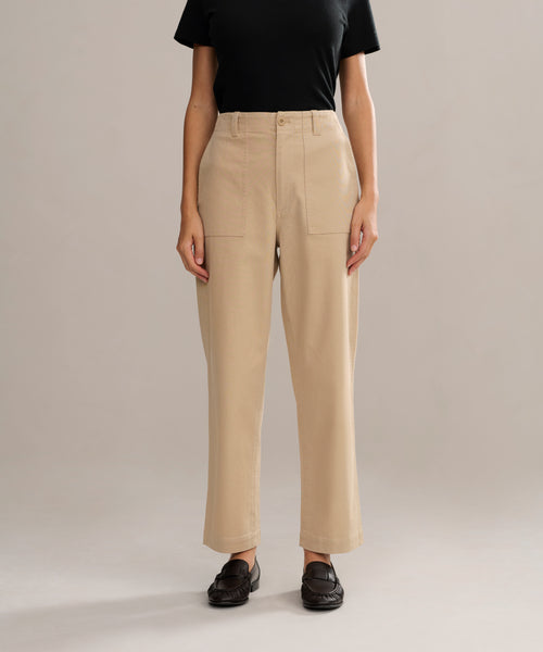 A person in a black short-sleeve shirt, Ranger Trouser in beige with front pockets and a fitted silhouette, and black loafers stands against a plain beige background.