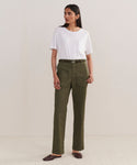 A woman stands against a plain background wearing a white t-shirt tucked into high-waisted Relaxed Army Pants with a belt and large pockets, paired with dark brown flat shoes.