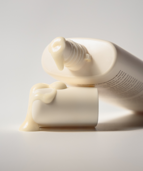 A close-up of the Cleanse and Polish Duo shows an open cream tube with a beige formula on the white cap, set against a light background—ideal for achieving a fresh-faced glow or enhancing your cleansing and exfoliating routine.