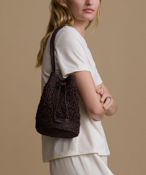 Model holding a brown raffia bucket bag against a beige background.