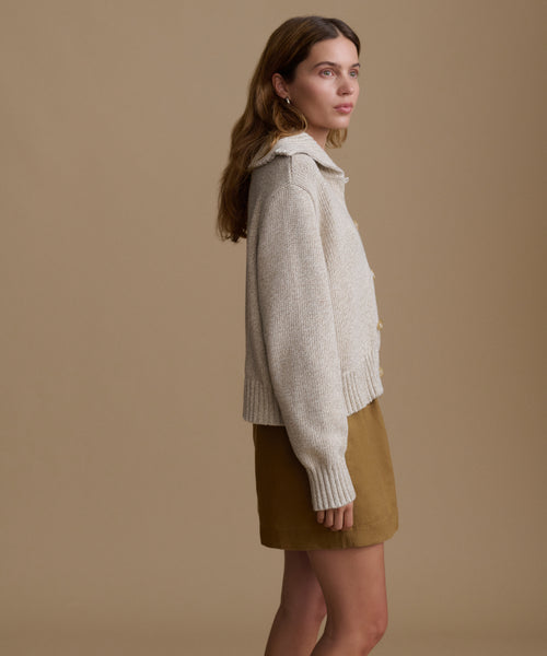 Woman wearing a beige sweater and brown shorts against a beige background