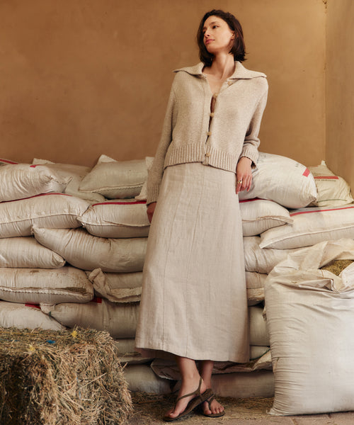 Woman in a beige outfit standing among stacked sacks with a neutral background