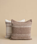 Two textured throw pillows with horizontal stripes, one in taupe and cream and one in off-white and taupe, set against a solid beige background.