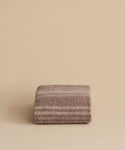 The Sheridan Throw, crafted from a soft alpaca blend yarn in brown and beige stripes, is elegantly folded and displayed against a plain beige background.