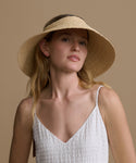 Woman wearing a straw visor hat against a beige background
