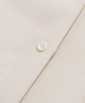 Close-up of the Silk Sloane Shirts sandwashed silk fabric, featuring a shiny white button sewn on. The material looks smooth and soft, with detailed stitching around the button.