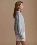 Woman wearing a light blue v-neck sweater with blue and white stripe shorts against a brown wall. 