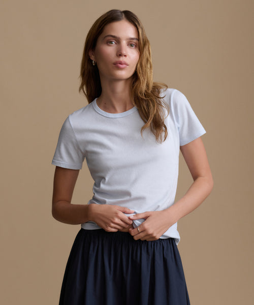 Woman wearing a baby blue t-shirt and navy pants against a brown background.