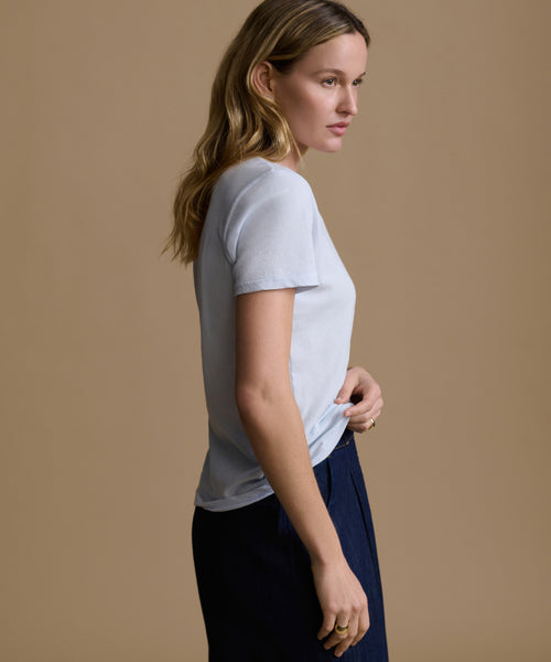 Woman wearing a baby blue t-shirt and navy pants against a brown background.