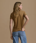 Woman wearing a brown top and blue jeans against a beige background