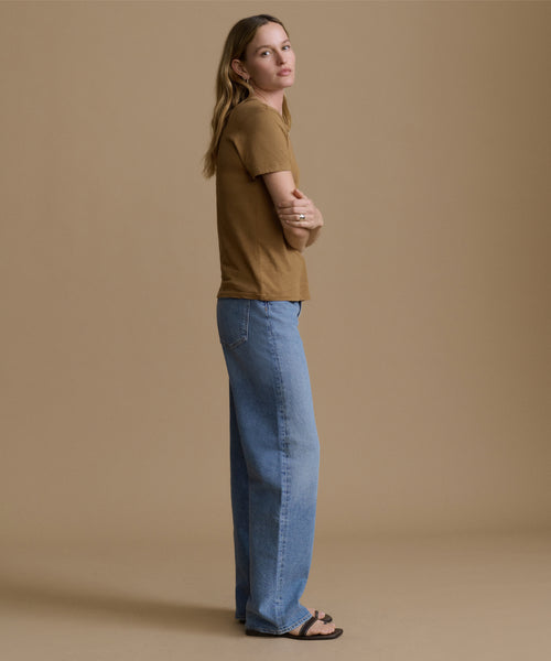 Woman wearing a brown top and blue jeans against a beige background
