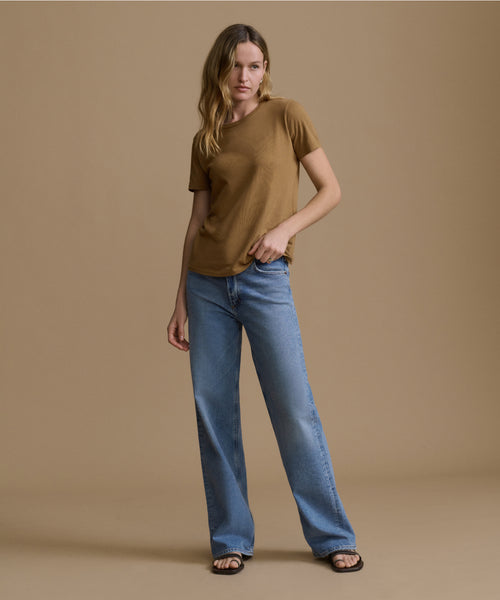 Woman wearing a brown top and blue jeans against a beige background