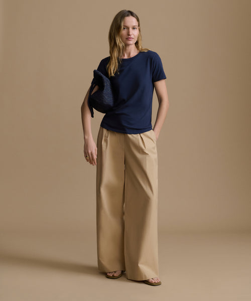 Woman wearing a navy blue t-shirt and beige pants on a brown background
