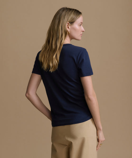 Woman wearing a navy blue t-shirt and beige pants against a brown background