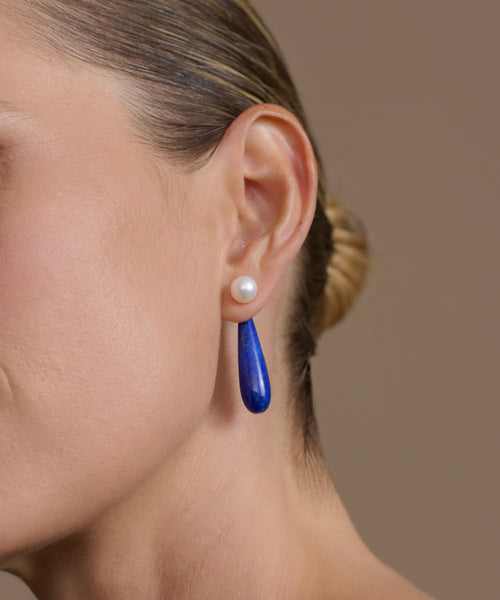 Close-up of a woman's ear wearing small angelika earrings on a neutral background