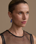 Woman wearing small angelika earrings and a sheer black top with a plain background