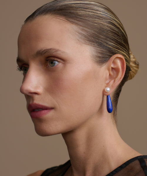 Close-up of a woman wearing small angelika earrings on a neutral background