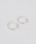 The Small Clara Hoops, crafted in sterling silver with post backings, are displayed on a light, textured fabric surface.