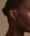 Close-up of a person’s ear and cheek wearing Small Eloise Hoops, set against a neutral background with their hair pulled back.