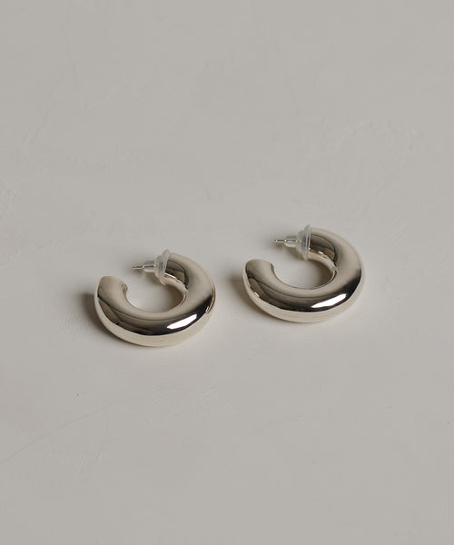 The Small Donut Hoops are chunky sterling silver earrings with clear backings, shown on a light gray textured surface.