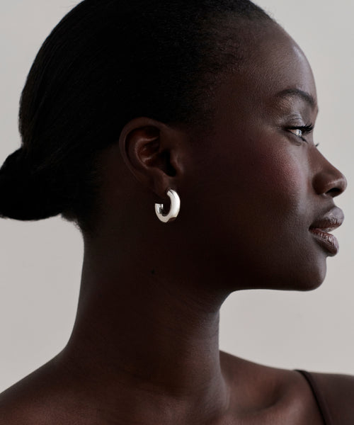 A woman with dark skin and short, pulled-back hair wears Small Donut Hoops and a thin strap top, shown in profile against a plain light background.