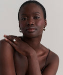 A confident, dark-skinned woman with short hair wears sculptural jewelry, including Small Donut Hoops in sterling silver, a ring, and a thin strap top. One arm rests gracefully across her shoulder against a plain background.