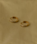 The Stevie Grey Diamond Hoops, crafted in 14k gold and inspired by heirloom styles, rest on smooth beige fabric. Delicate grey diamonds add subtle sparkle to these timeless earrings.