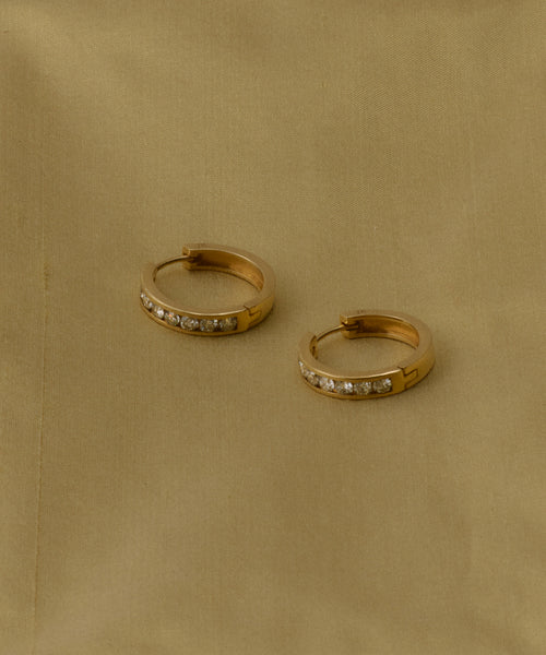 The Stevie Grey Diamond Hoops, crafted in 14k gold and inspired by heirloom styles, rest on smooth beige fabric. Delicate grey diamonds add subtle sparkle to these timeless earrings.
