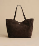 The Suede Agnes Tote is a spacious, dark brown bag with two handles—ideal as a stylish laptop tote. Shown on a plain beige background.