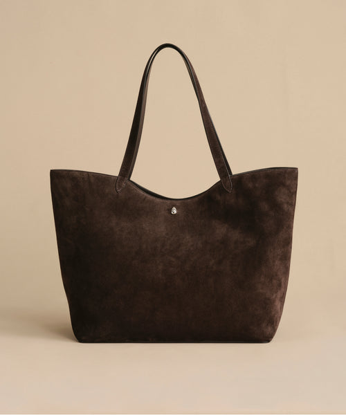 The Suede Agnes Tote is a spacious, dark brown bag with two handles—ideal as a stylish laptop tote. Shown on a plain beige background.