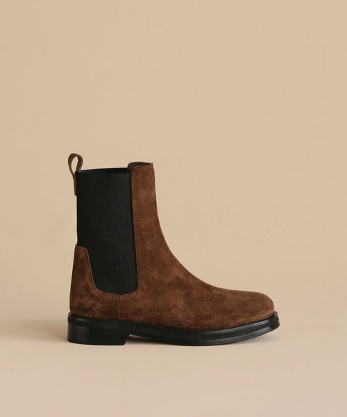 The Suede Alden Boot features brown suede, black elastic side panels, a back pull tab, and a weather-resistant rubber sole, shown on a beige background.
